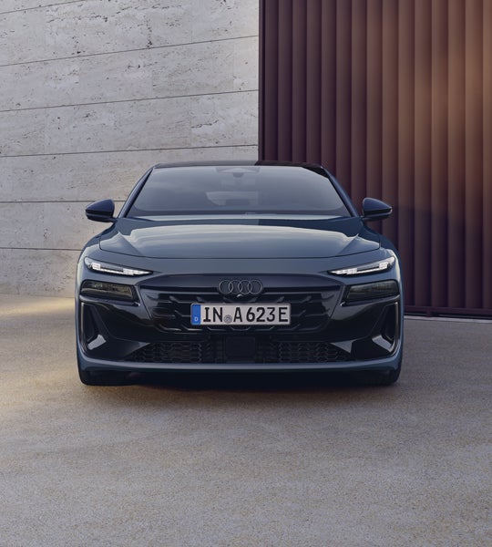 Frontprofil des A6 Sportback e-tron, welcher auf einem Betonuntergrund vor einer Gebäudefassade steht.&nbsp;