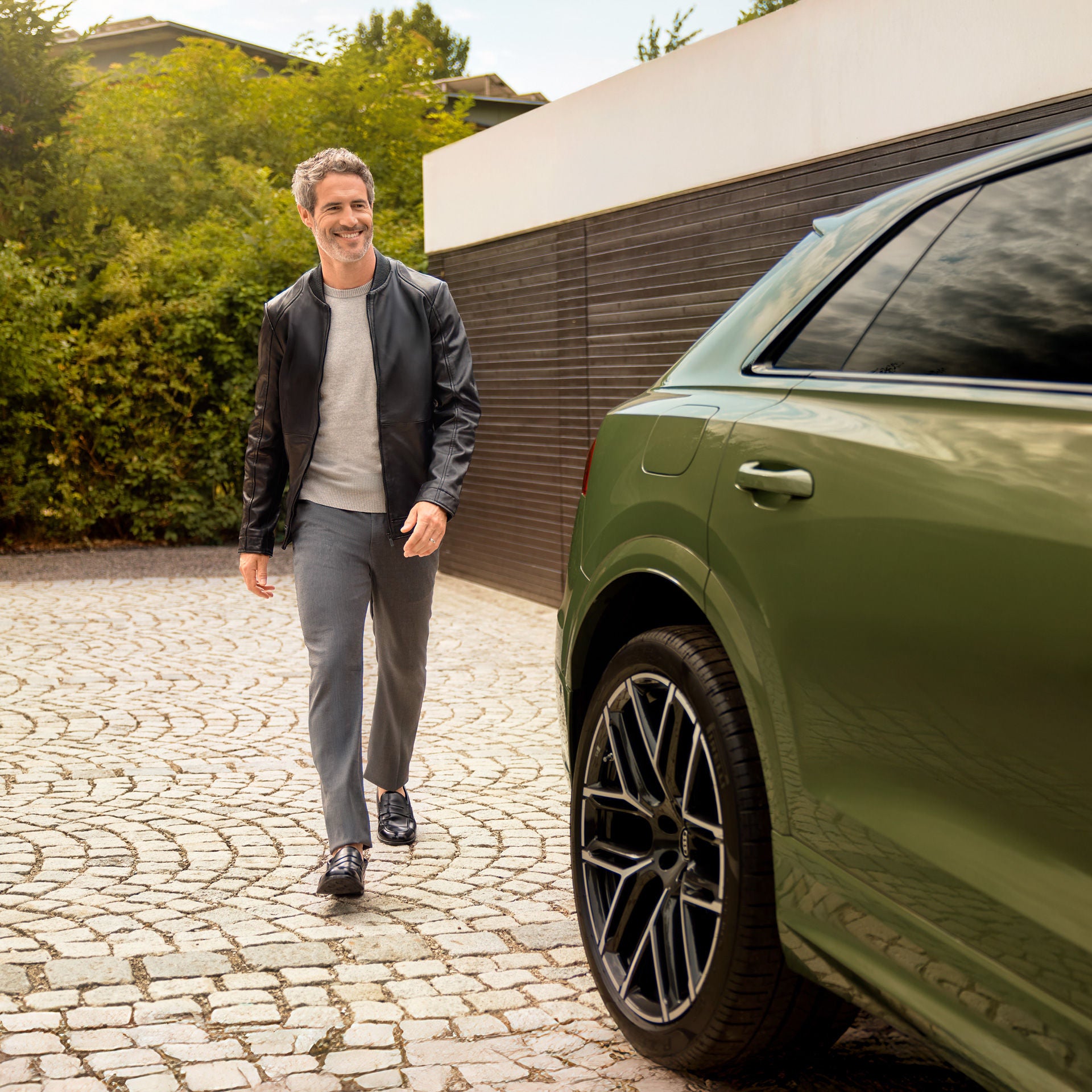 Ein Mann hat eine Hand an einer grünen, offenstehenden Autotür und lächelt zur Seite gerichtet.