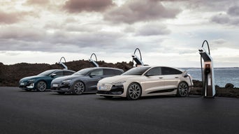 Dark grey Audi Q6 Sportback e-tron charging at a charging station in a wooden-roofed charging station.