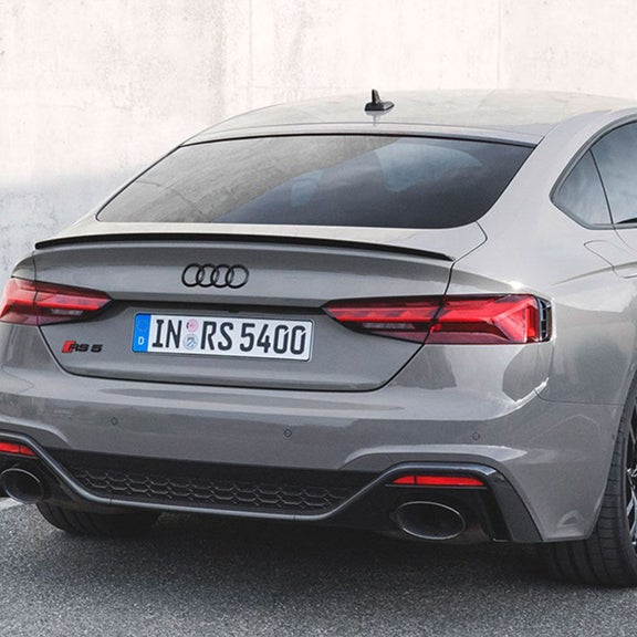 Rear view of a parked Audi RS5 Sportback in grey, near a concrete wall.
