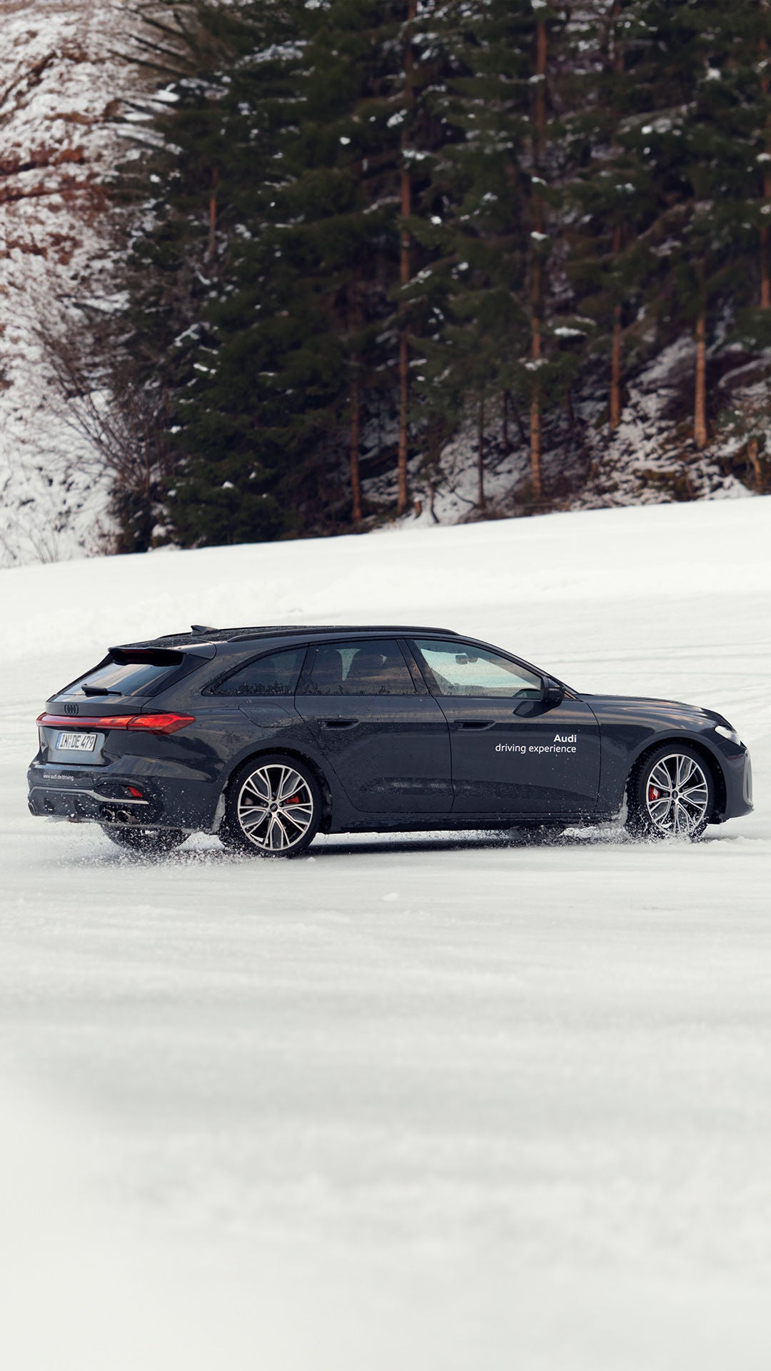Dunkler Audi S5 Avant mit weißem Schriftzug „Audi driving experience“ driftet über schneebedeckte Fläche.