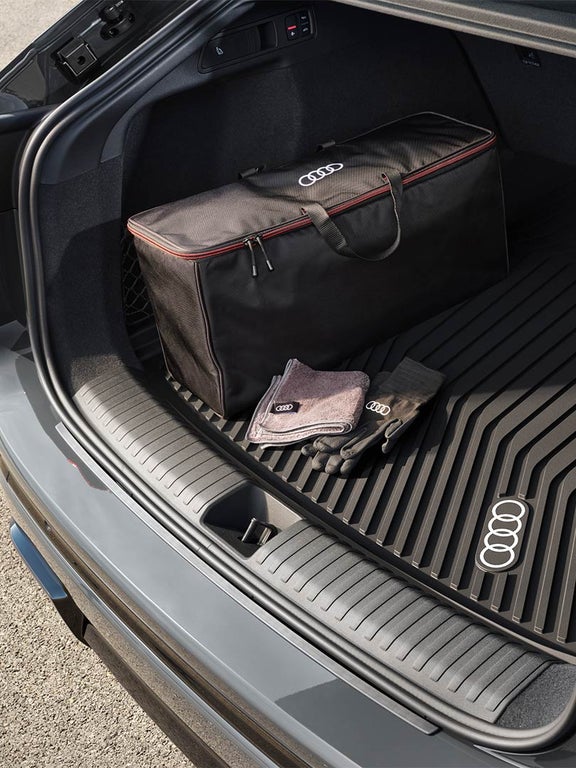 Kofferraum eines Audi Q6 Sportback e-tron mit schwarzer Audi Tasche, Audi Handschuhen und Audi Tuch auf Gummimatte.