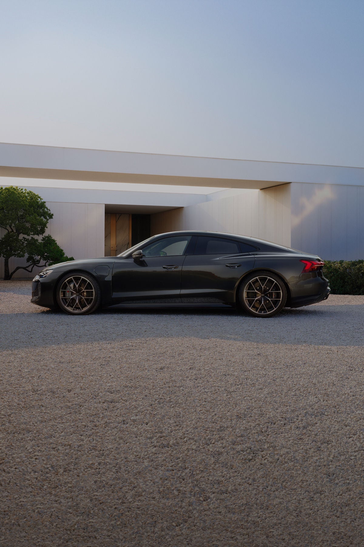 Audi e-tron GT side view on gravel surface in front of a house