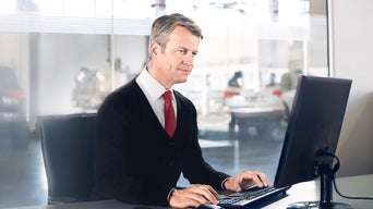 Businessperson typing at desk with Audi car blurred in background through glass