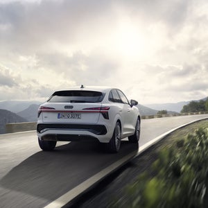 Una Q3 Sportback e-hybrid bianca guida su una strada di campagna in un paesaggio montuoso.