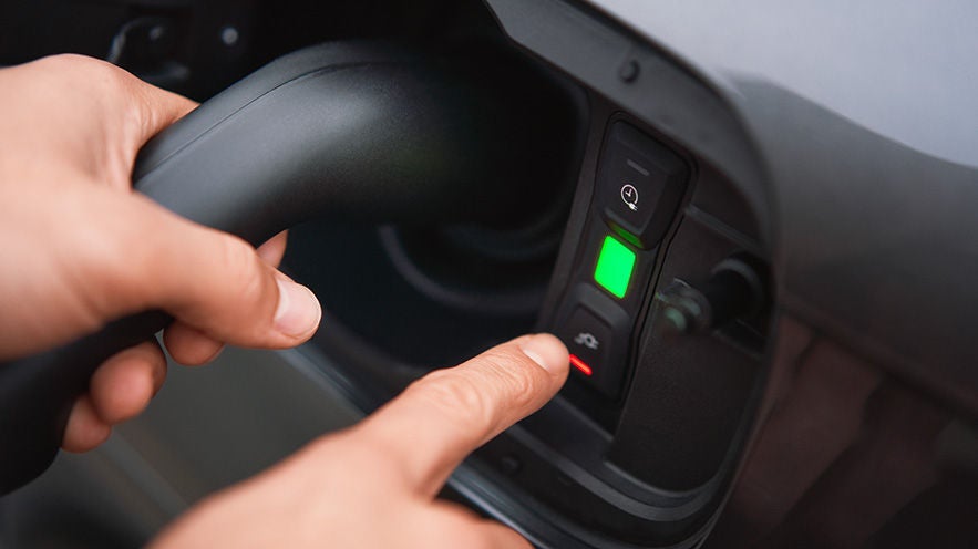 Nahaufnahme einer Hand, die einen Ladevorgang an einem Elektrofahrzeug startet oder beendet, grüne LED-Leuchte sichtbar.