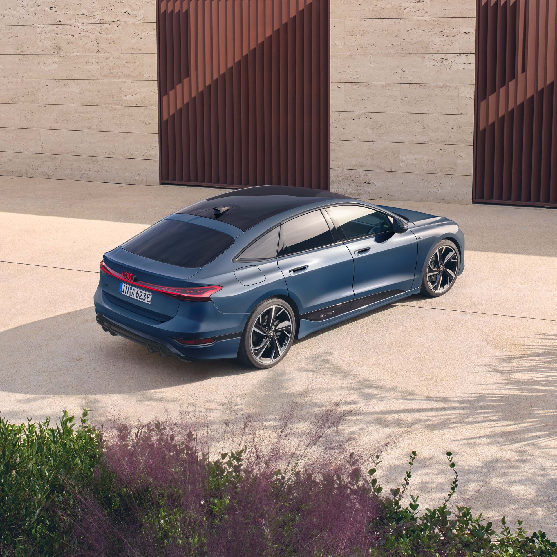 Blauer Audi A6 Sportback e-tron von schräg hinten, geparkt auf hellem Beton vor moderner Fassade.
