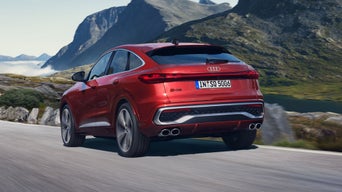 Schräges, hinteres Seitenprofil des roten SQ5 Sportback, welcher auf einer Straße durch die Berge fährt.