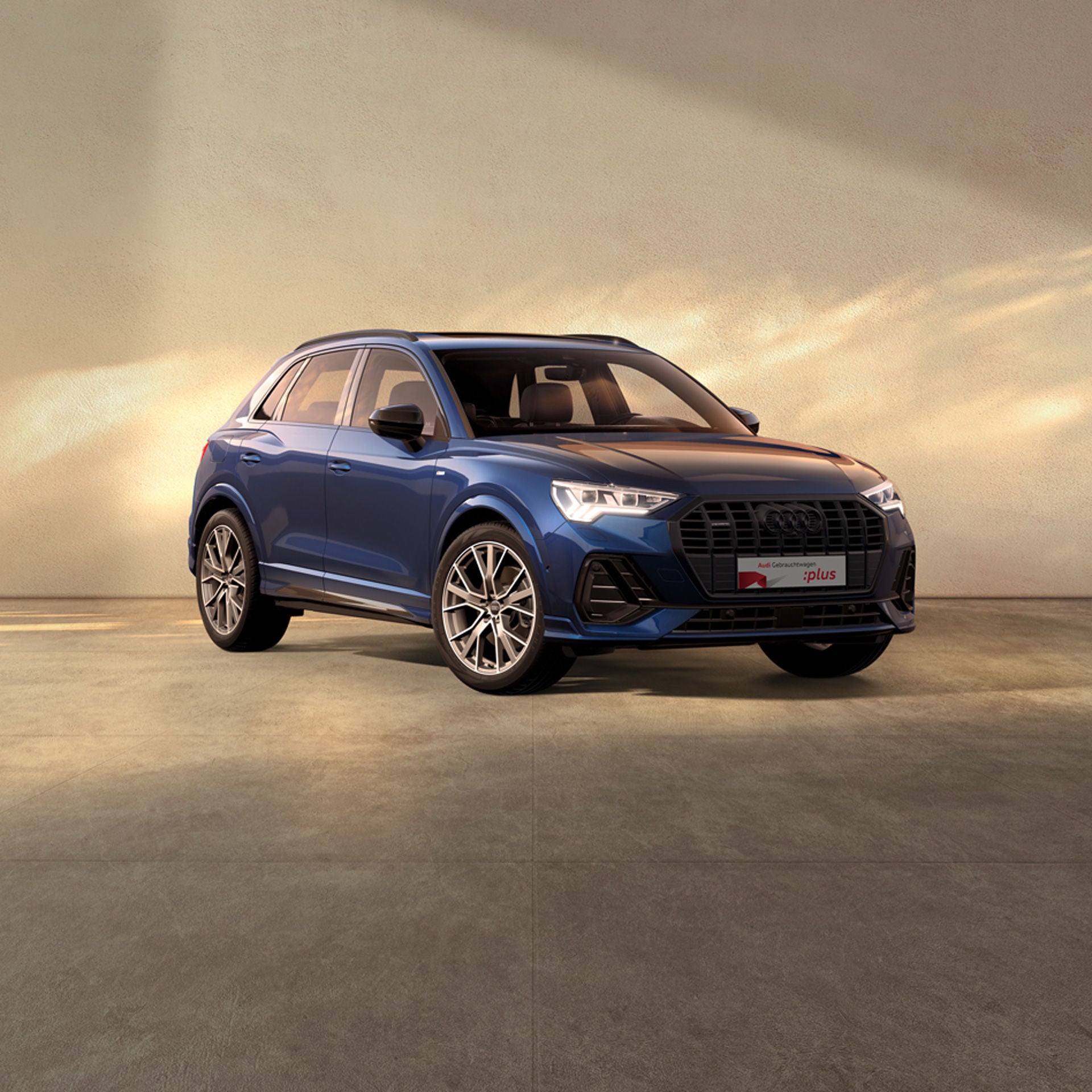 Ein blauer Audi Q3 steht auf einer beigen Fläche bei einfallendem Sonnenlich. Am Rand sind Kirschblüten zu sehen.