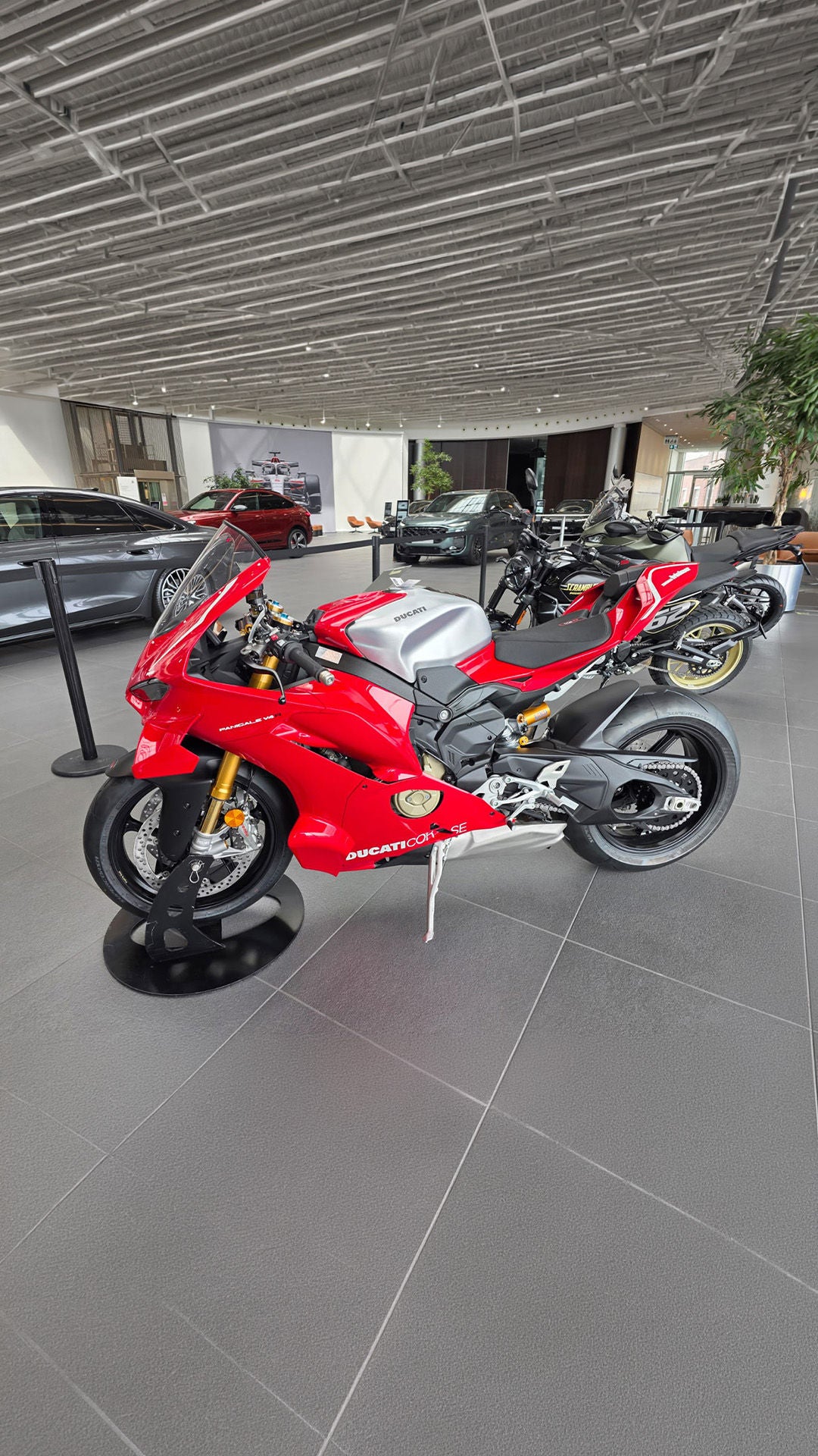 Rotes Ducati-Sportmotorrad im Showroom, umgeben von Autos und weiteren Motorrädern.