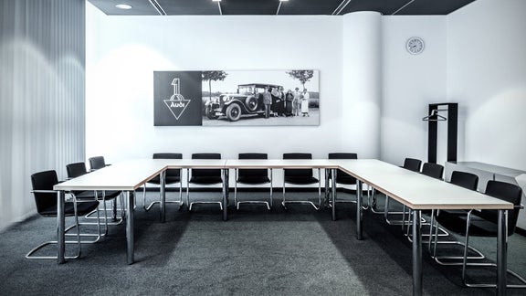 Besprechungsraum mit U-förmigem Tisch, schwarzen Stühlen und historischem Audi-Foto an der Wand.