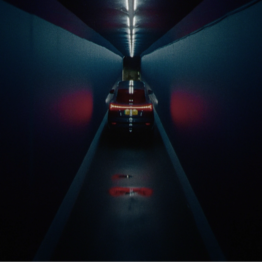 Rear view of the Q6 Sportback e-tron driving down a dark, narrow futuristic tunnel lit by overhead ceiling lights