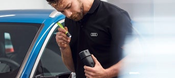 An Audi mechanic inspecting a part from an Audi vehicle with a torch