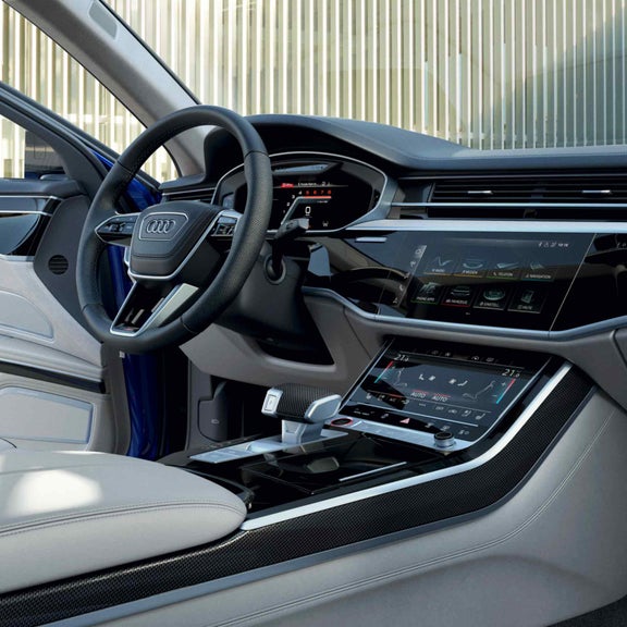 Frau öffnet die Fahrertür eines Audi S8 TFSI, Innenraum mit hellem Leder, Lenkrad und zentralem Touchscreen sichtbar.