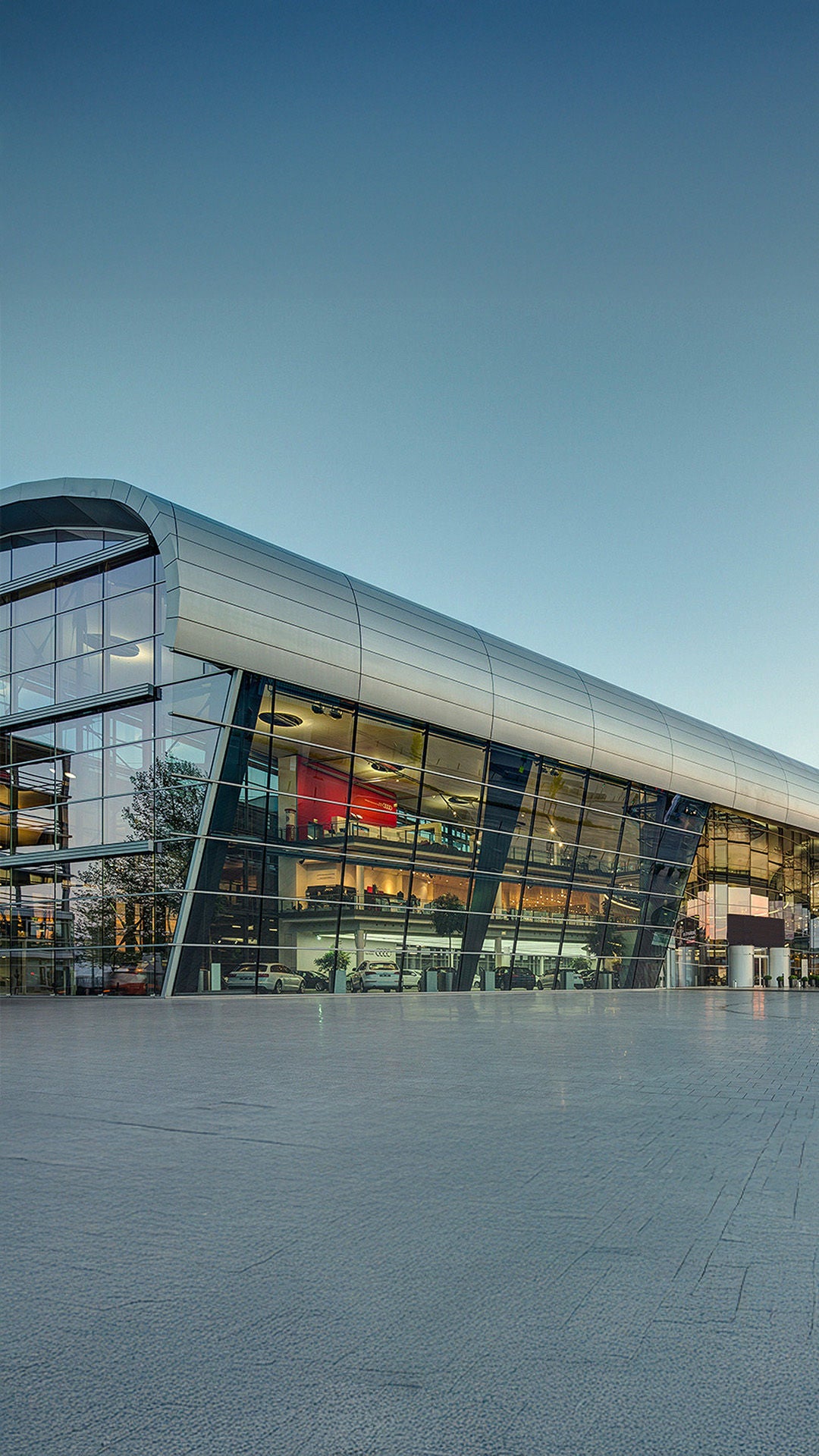 Moderne Glasfassade des Audi Forums Neckarsulm bei Tageslicht mit sichtbaren Fahrzeugen im Inneren.