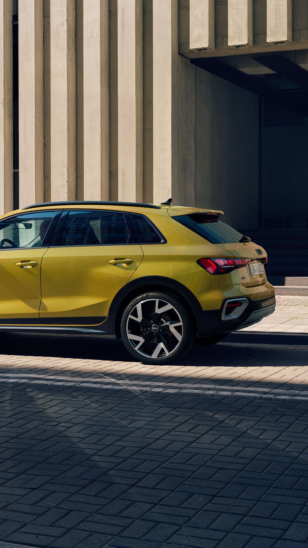 Gelber Audi A3 steht am Straßenrand vor moderner Fassade, eine Frau in gelbem Outfit geht auf dem Gehweg daneben entlang.