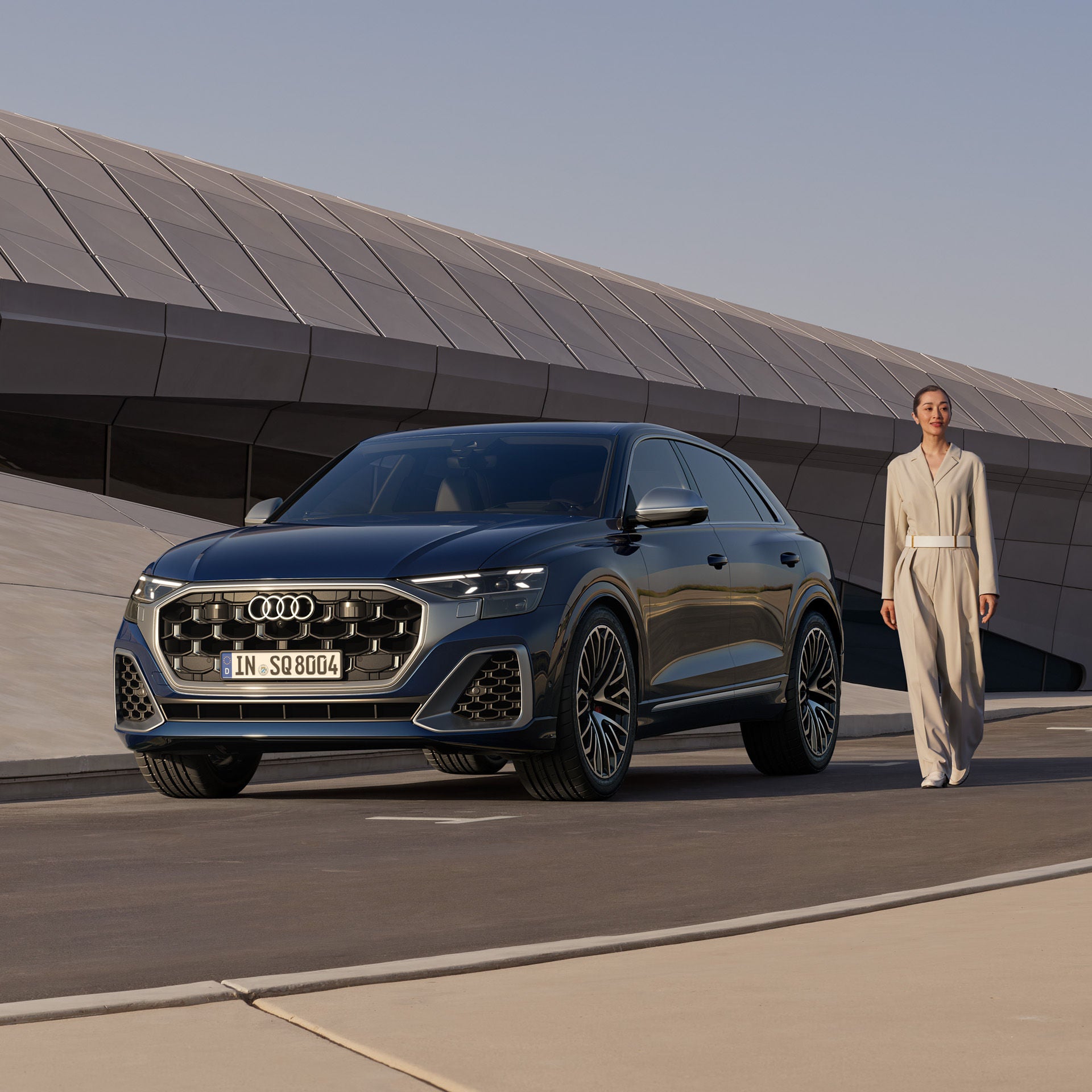 Eine Frau steht neben einem geparkten, dunkelblauen Audi SQ8 SUV vor einem modernen Gebäude.