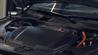 Geöffnete Motorhaube eines Elektroautos mit sichtbaren orangefarbenen Hochvoltkabeln.