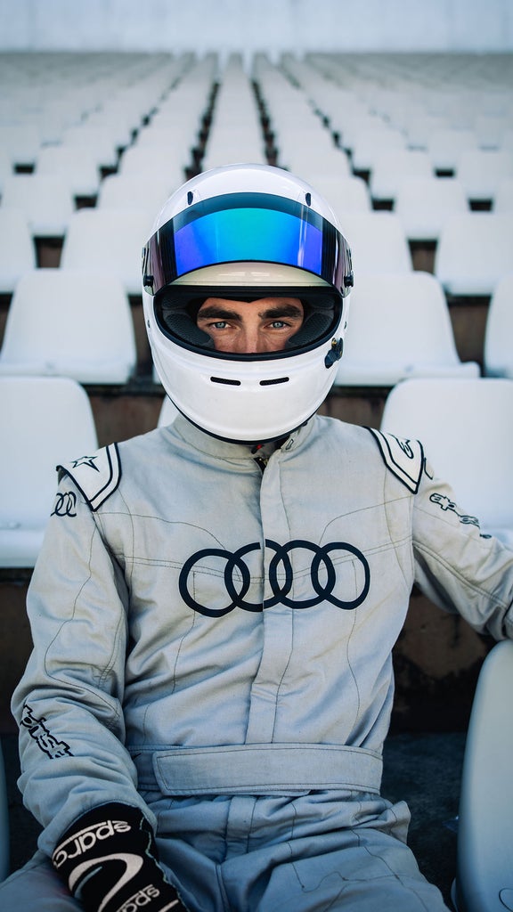 Der Rennfahrer von TUfast hat einen Helm auf, sitzt auf einer leeren Tribüne und ist zur Kamera gerichtet