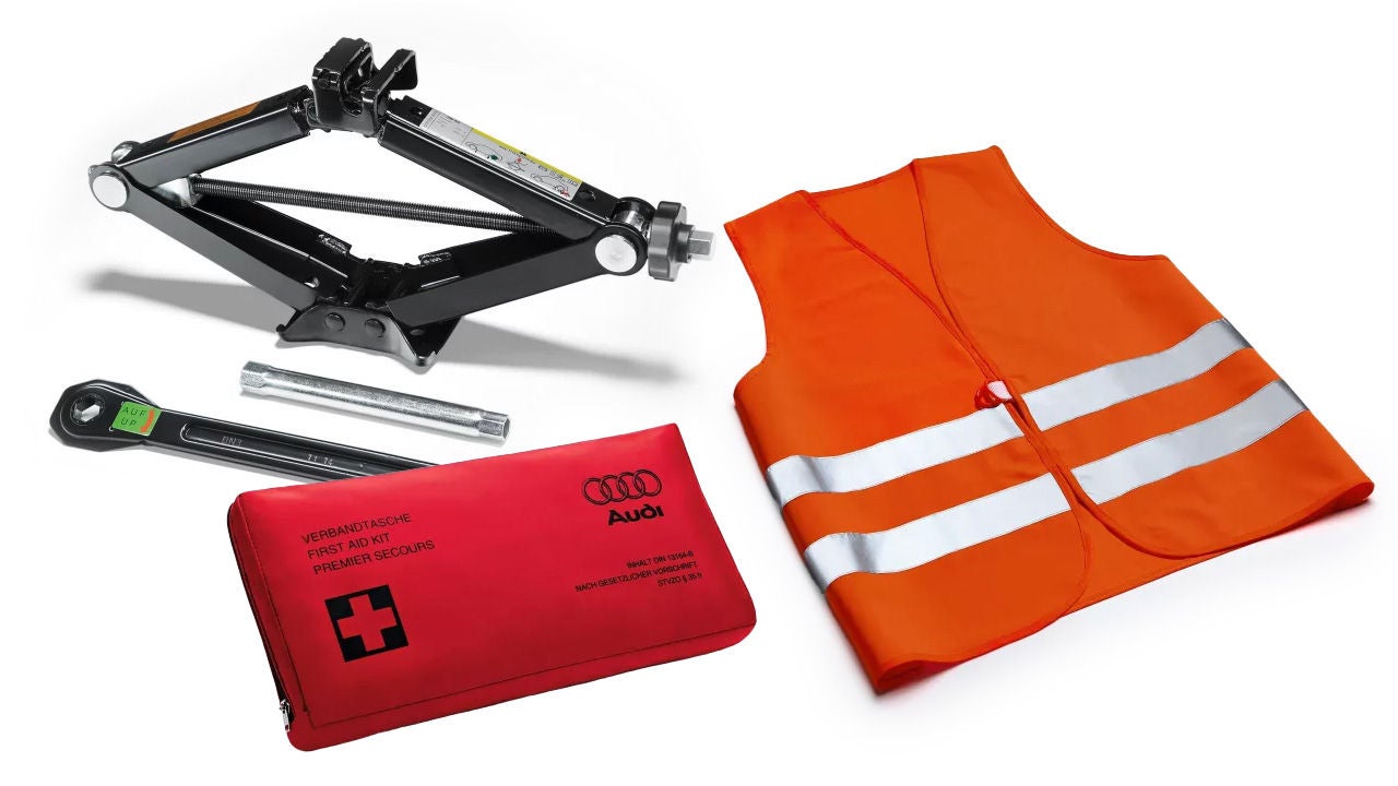 Notfallset mit Warndreieck, Warnweste, Verbandtasche, Radkreuz und Wagenheber auf weißem Hintergrund.
