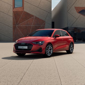Ein roter Audi A3 Sportback steht schräg vor einem modernen Gebäude