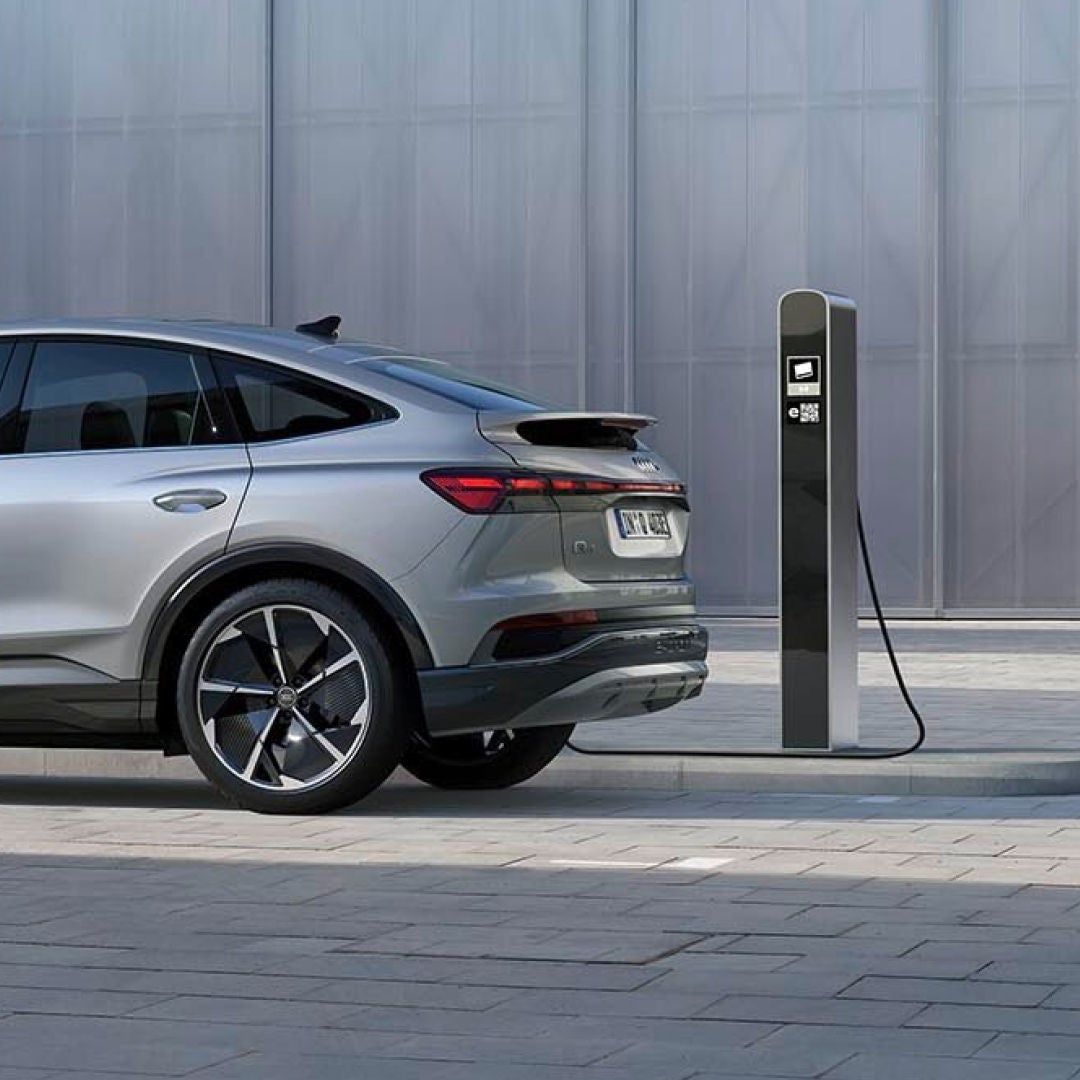 A silver Audi electric vehicle parked at a charging station against a modern architectural backdrop.