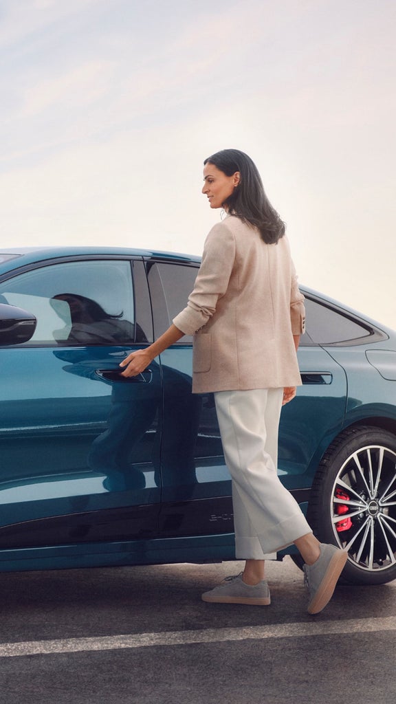 A person walking past a parked silver Audi Q7 vehicle near a corrugated metal wall