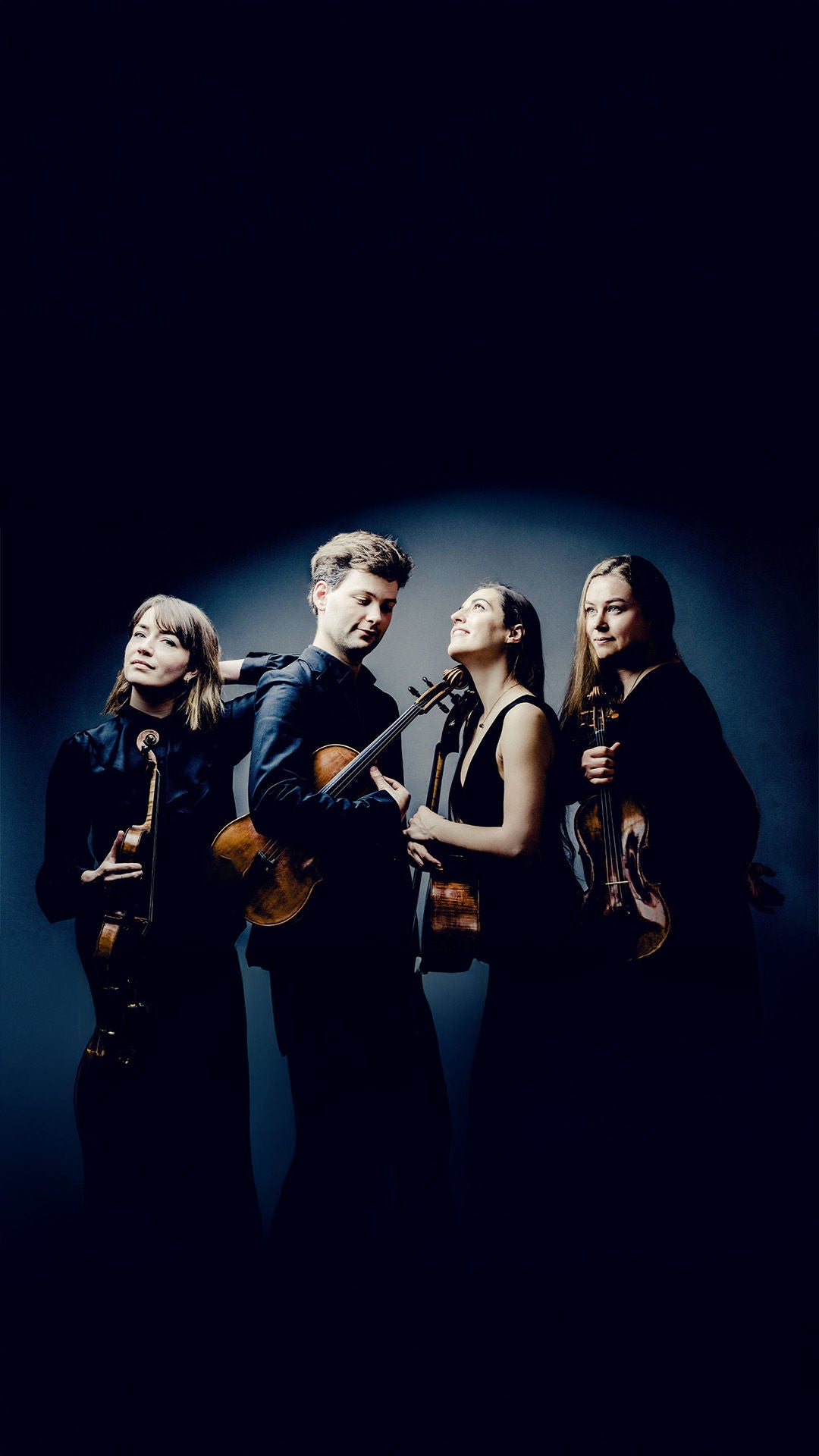 Vier Musikerinnen und Musiker mit Streichinstrumenten posieren im Studio vor dunklem Hintergrund, schwarze Kleidung.