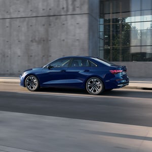 Audi A3 sedan, sedd från sidan på en stadsgata. Bakom bilen syns en modern byggnad med fasad i betongkänsla.