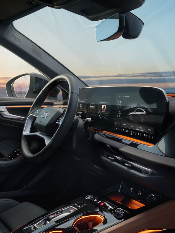Cockpit des Audi A5 Avant mit großem Curved-Display, Ambientebeleuchtung und Sonnenuntergang im Hintergrund.