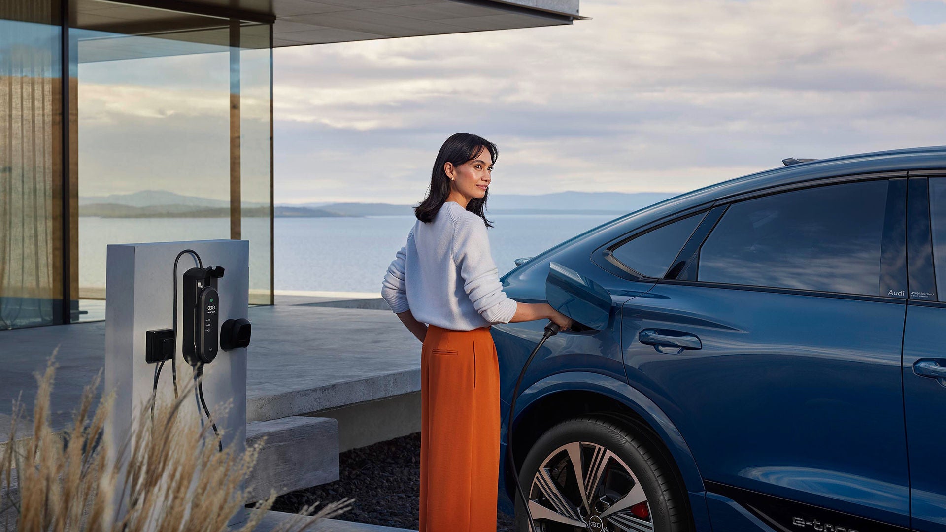 Ein blauer SQ6 SB e-tron steht vor einem Haus und wird von einer Frau geladen