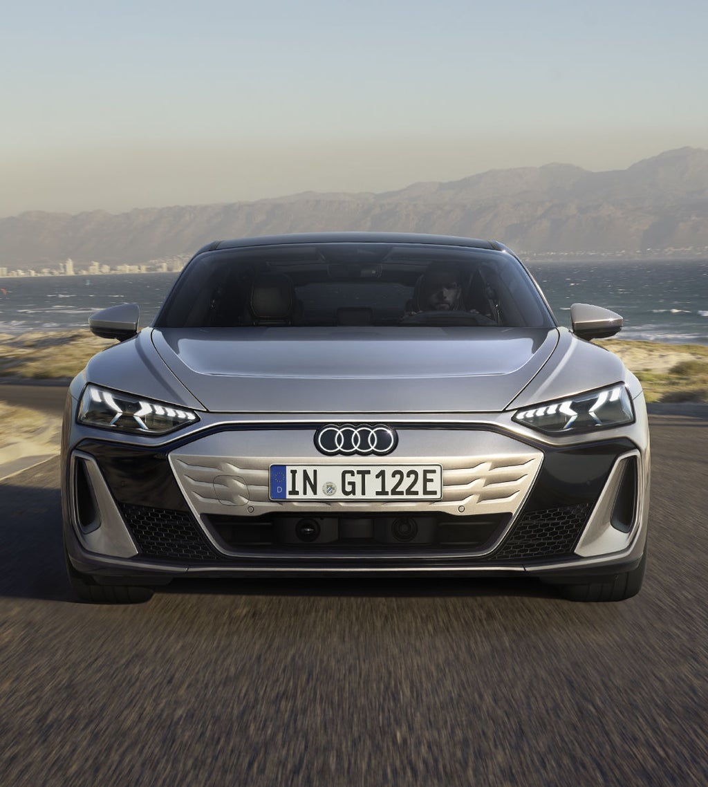Die Frontansicht des Audi S e-tron GT auf einer kurvigen Küstenstraße. Die markanten LED-Scheinwerfer und das geschlossene, aerodynamische Kühlergrill-Design sind erkennbar.