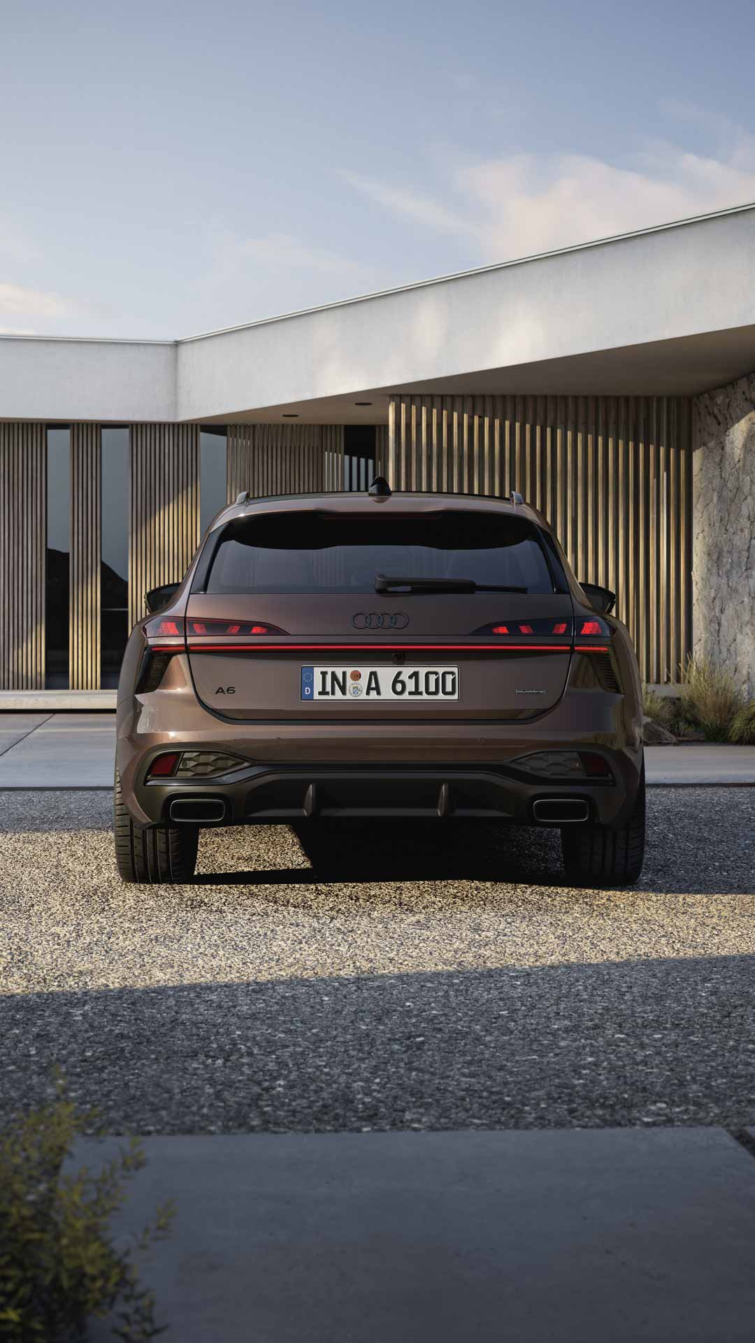 Heckaufnahme des A6 Avant, der auf einer Kiesfläche vor einer Fassade mit Holzvertäfelung und hohen Fenstern steht.