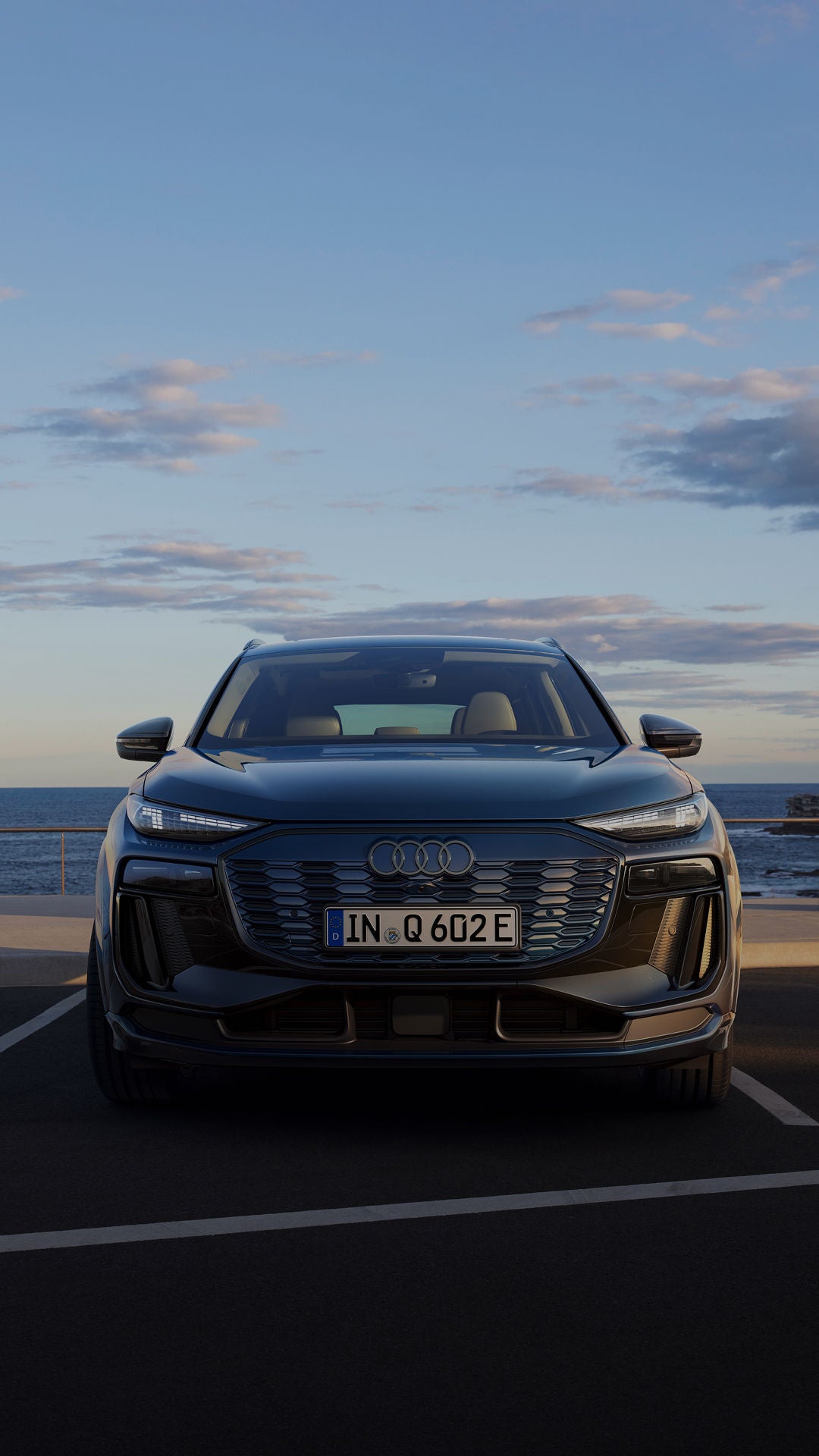 A new blue Audi Q6 e-tron SUV e-tron parked beside the ocean, showcasing its sleek design against a scenic coastal backdrop.