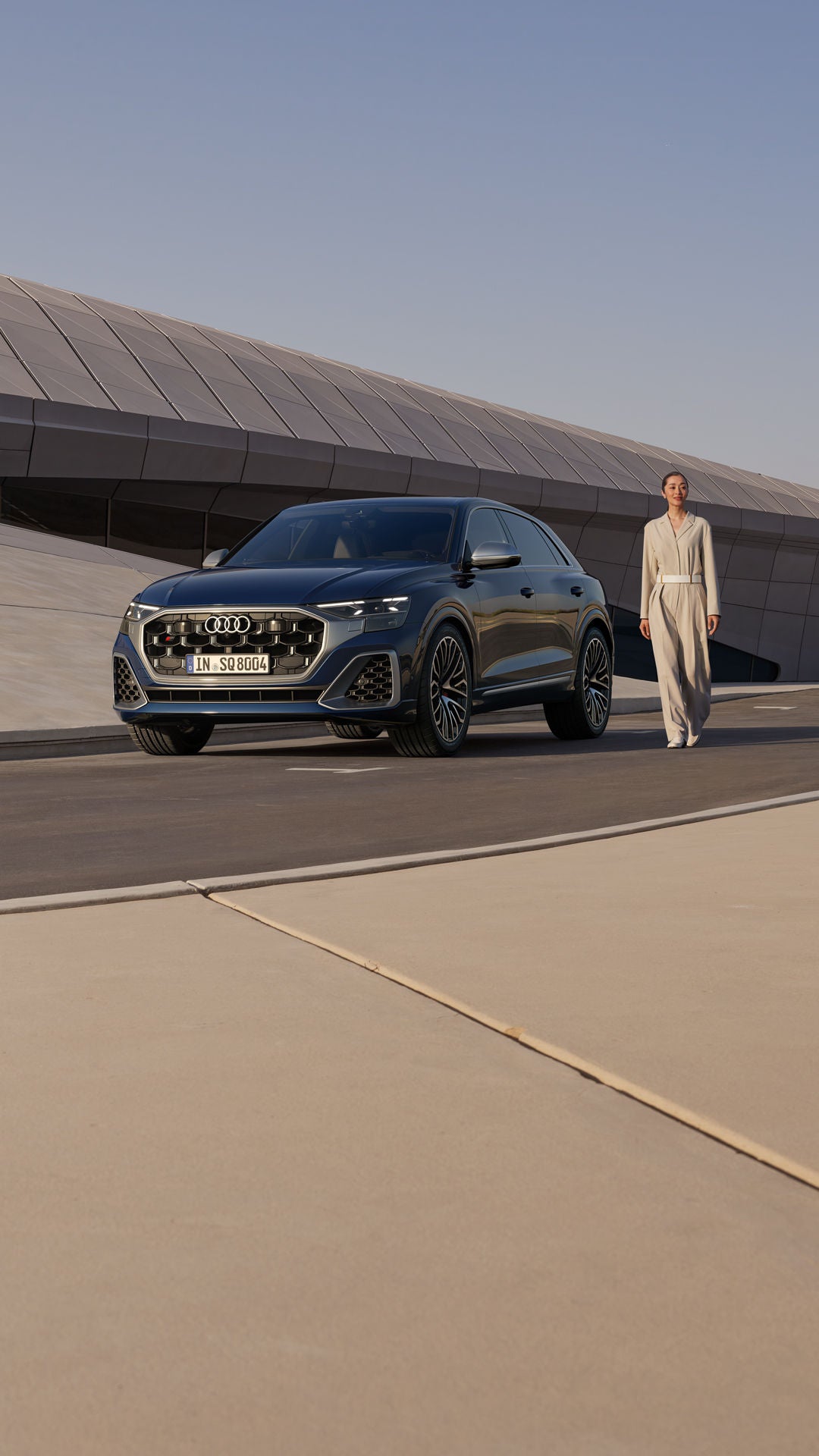 Der SQ8 SUV vor einem futuristischen Gebäude mit geschwungener Form parkend, daneben eine modisch gekleidete junge Frau.