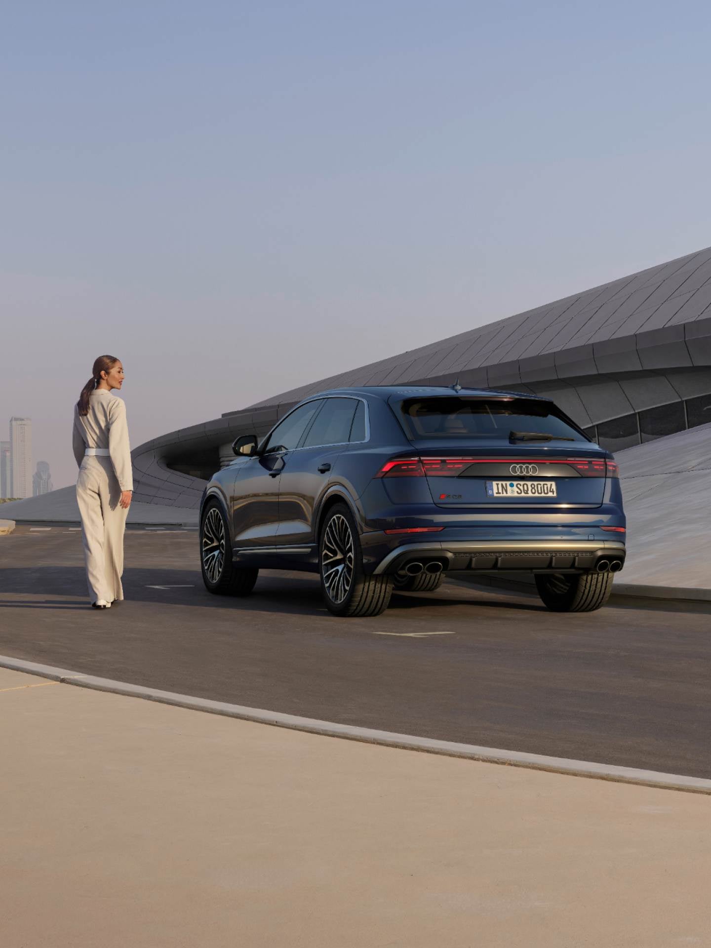 Lady looking over her shoulder at parked Audi SQ8 near modern building.