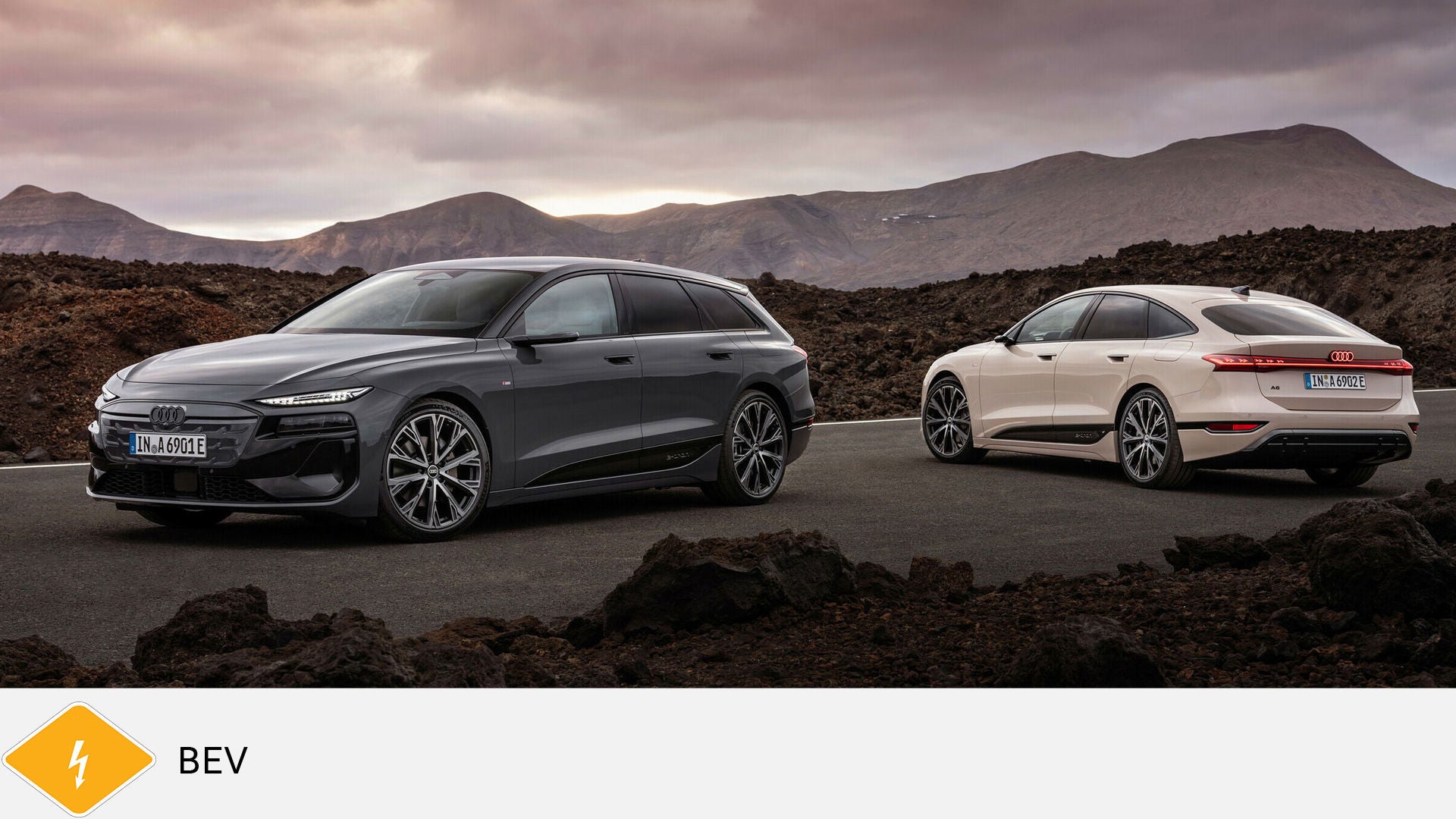 Two Audi A6 e-tron are standing on a volcanic road against a mountain backdrop, gray and white. Yellow BEV symbol with lightning bolt at the bottom.