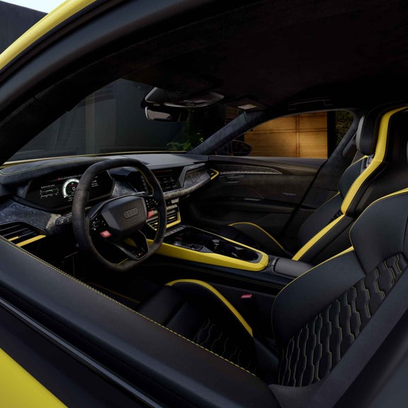 Innenraum eines gelben Audi RS e-tron GT performance mit schwarzem Leder, gelben Akzenten und digitalem Cockpit, aufgenommen durch die offene Tür.