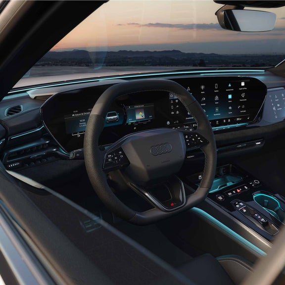 Blick durch das Seitenfenster eines Audi A5 Avant e-hybrids in den Innenraum auf das Lenkrad und das Audi virtual cockpit, das MMI und das Passenger Display.