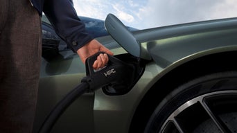 A person holding a charging connector to an electric vehicle's charging port, showcasing sustainable energy usage.