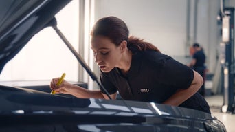 Une femme se penche au-dessus du compartiment moteur d'un véhicule et examine quelque chose.