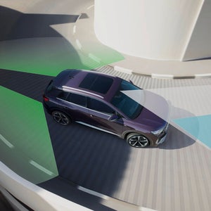 Aerial view of a purple SUV using driver assistance technology. Green and blue overlay visuals depict the car's sensor range on a circular road.