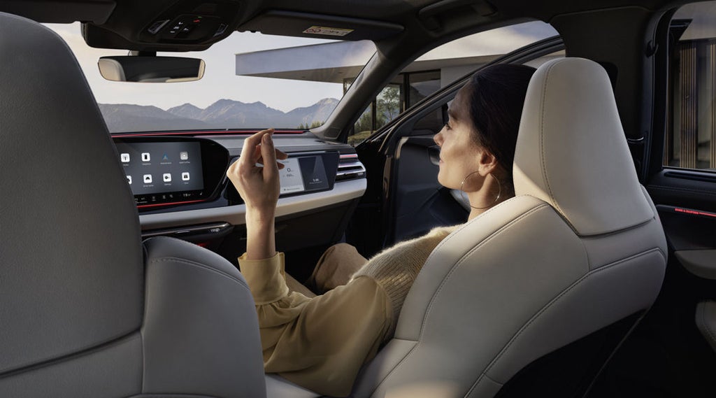 Vy från baksätet i en A6 Avant av en ung kvinna som sitter i passagerarsätet med dörren öppen. I bakgrunden syns berg.