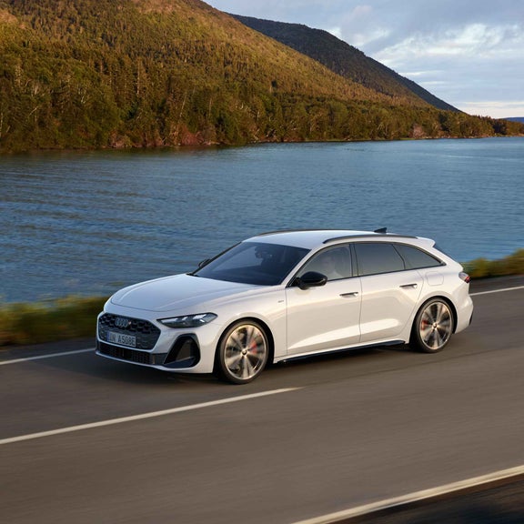 Ein weißer Audi A5 Avant e-hybrid fährt auf einer Straße an einem See entlang. Im Hintergrund ist das andere Ufer mit Bäumen zu erkennen.