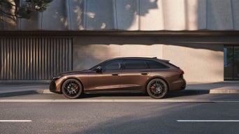 Un Audi A6 Avant marron est garé dans une rue devant un bâtiment moderne.