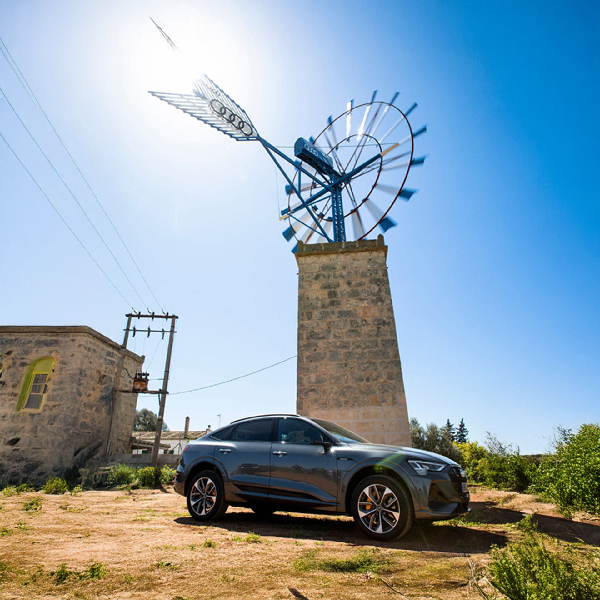 An Audi e-tron stands in front of a Majorcan windmill with the four rings logo on its wing.