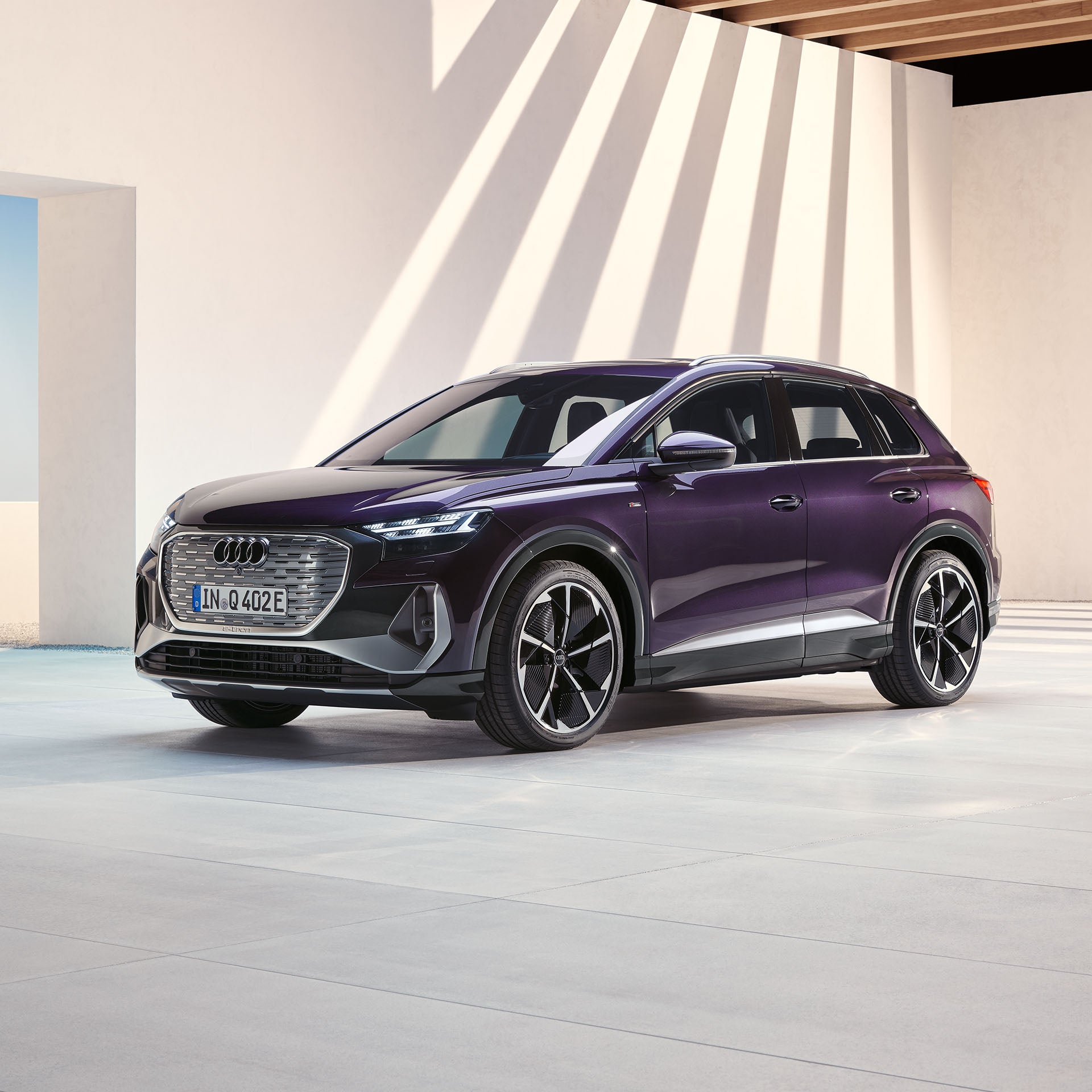 Violetter Audi Q4 e-tron steht in hellem, lichtdurchflutetem, modernem Innenhof mit Schattenspiel an der Wand.