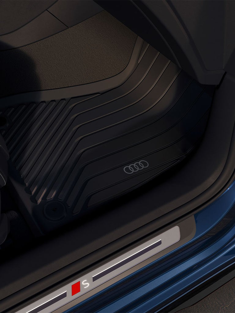 Detailansicht des Einstiegs einer Audi S5 Limousine mit schwarzer Sitzverkleidung, Gummifußmatte und beleuchtetem S-Logo.