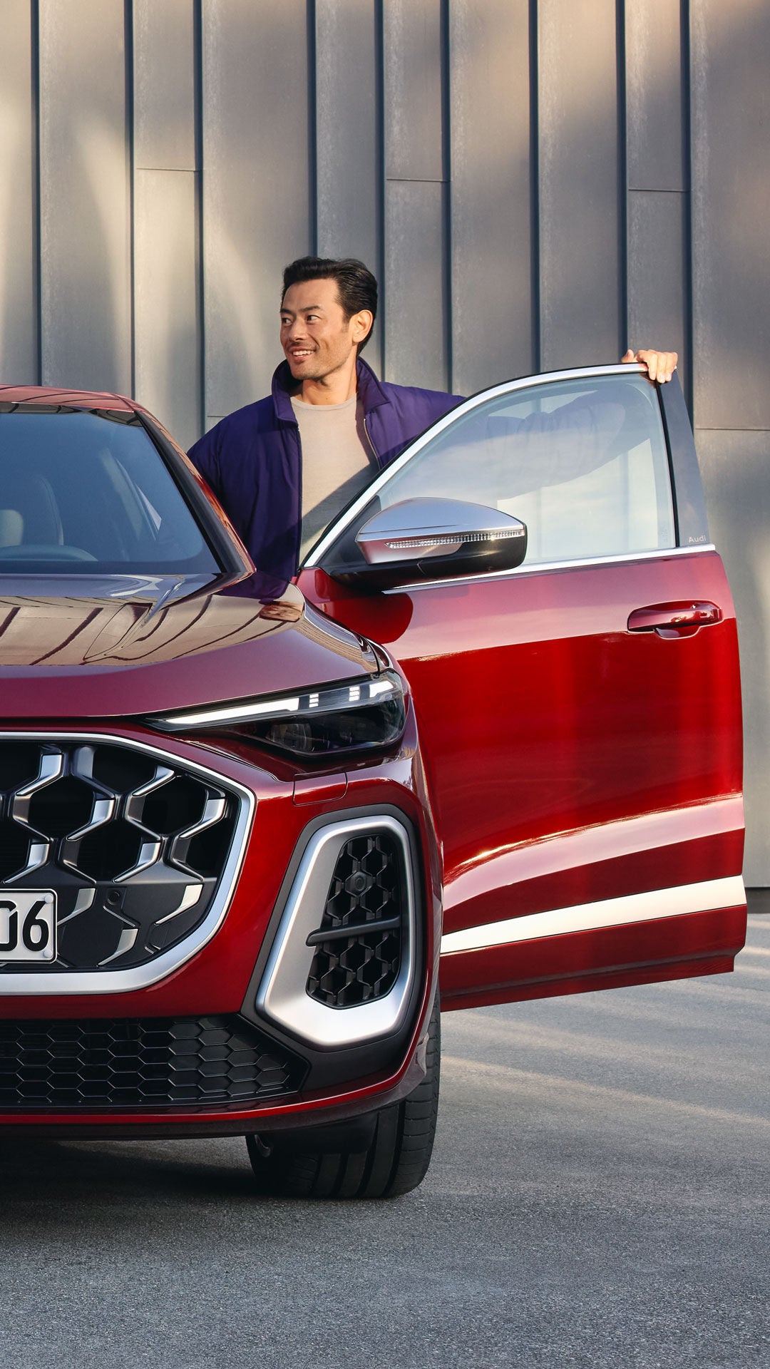 Ein Mann steigt aus einem roten Audi SQ5 vor einer modernen Gebäudefassade mit vertikaler Struktur.