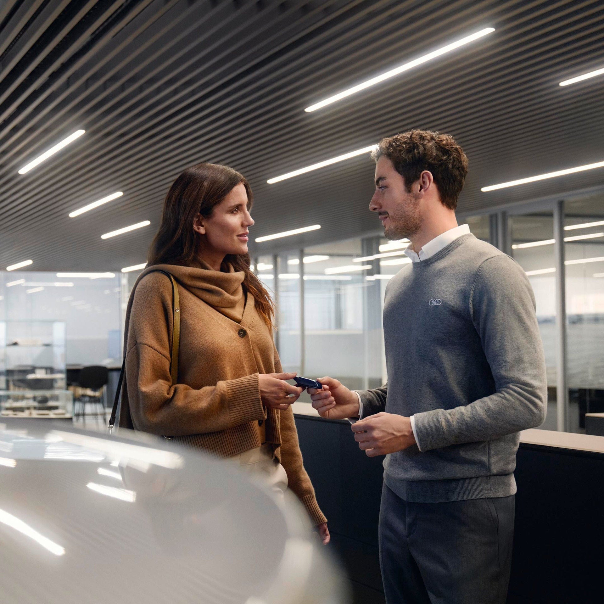 Mitarbeiterin und Kunde übergeben sich im Autohaus einen Autoschlüssel.